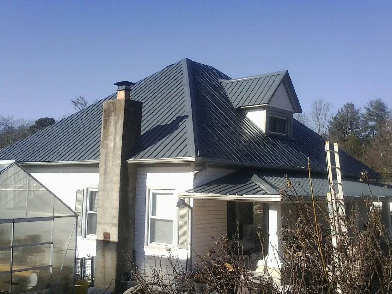 Dark blue standing seam metal roof on a white farmhouse with dormer — Slate & Tile Roof Repair by Roofing Brothers in Walsh