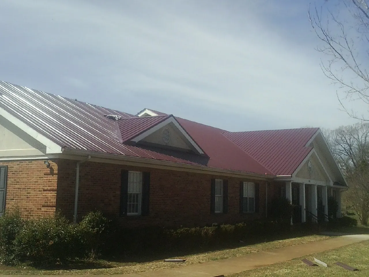 Red metal roof with gabled entries on a long brick building, from a Hail Damage Roof Repair job in Walsh