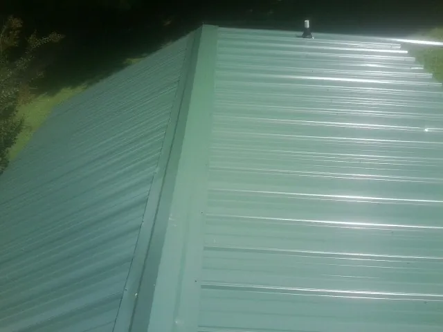 New green metal panels meeting at the ridge of a roof — Flat Roof Repair work by our crew in Walsh