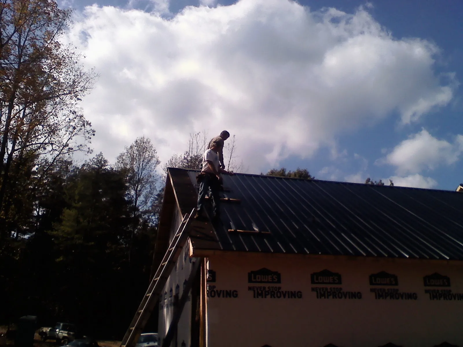 Roofer fastening dark metal panels high against a cloudy sky, from a Roof Inspection job in Walsh