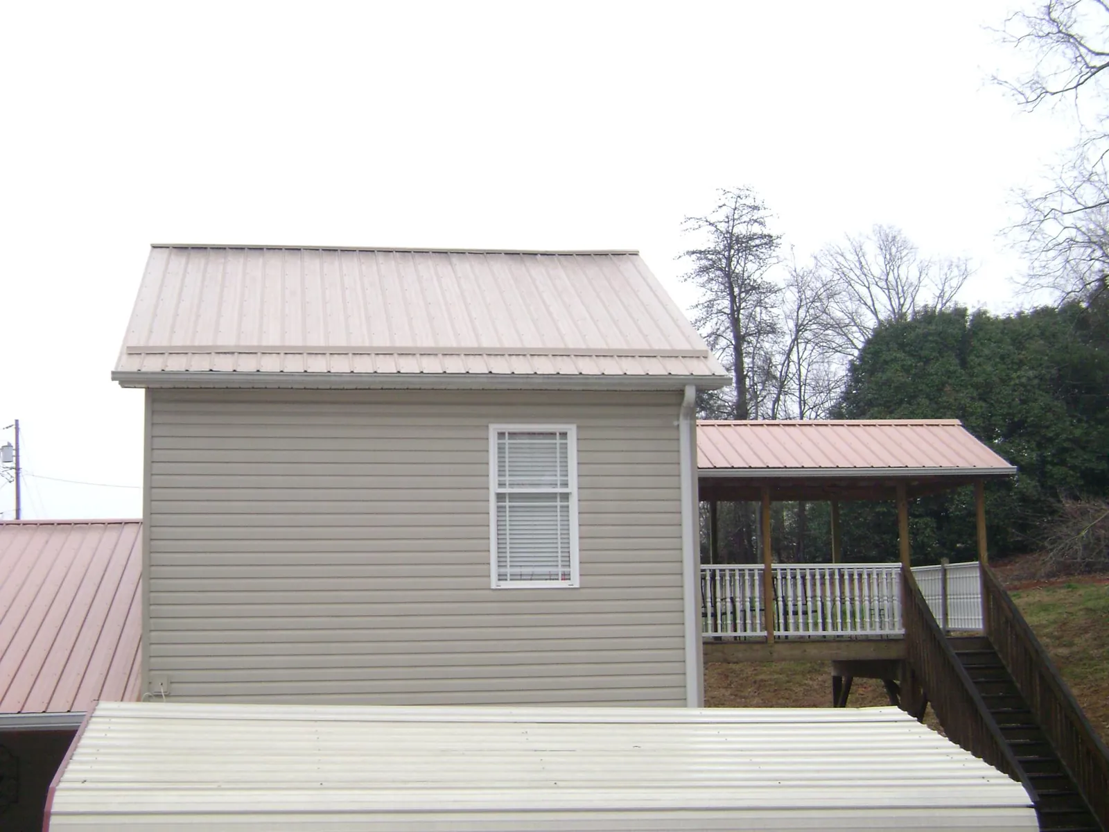 Tan metal roofs on a two story addition and attached porch, from a Roof Replacement job in Walsh
